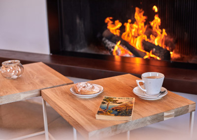 An espresso and an old Guía de Mallorca on an oak table in front of a lit fire