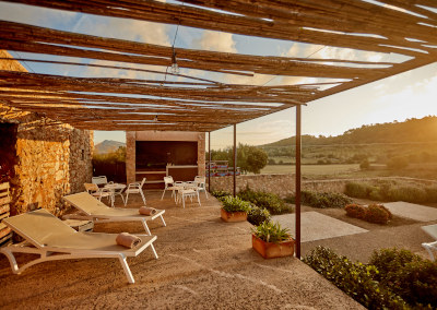 The courtyard terrace under its reed pergola at sunset, the low Mallorcan hills and cultivated fields stretching out beyond the wall