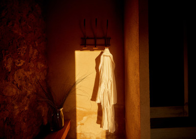 A white robe hung in a narrow shaft of warm light against rough limestone and lime plaster
